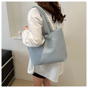 Close-up of a large light blue minimalist tote bag with wide straps worn by a model