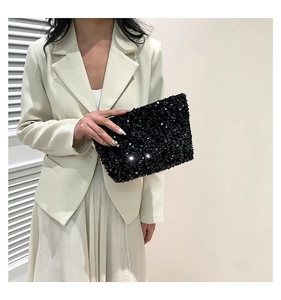 Elegant black sequin evening clutch bag held by model against a white dress background