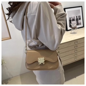 Detail of apricot saddle bag with golden bear-shaped lock and adjustable strap