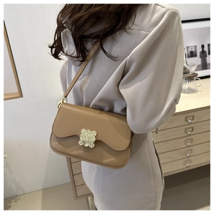 Detail of khaki saddle bag featuring a golden bear-shaped metal buckle and flip cover