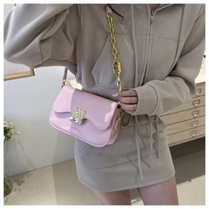 Detailed view of pink patent leather saddle bag with bear buckle and gold chain strap