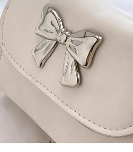 Détail du sac à main carré crème avec n'ud métallique argenté et coutures précises