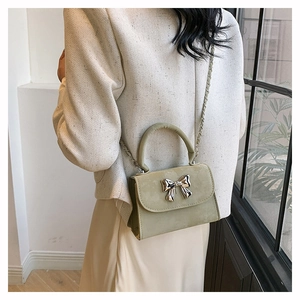Sac à main vert sauge avec boucle nœud argenté porté par un mannequin en tailleur