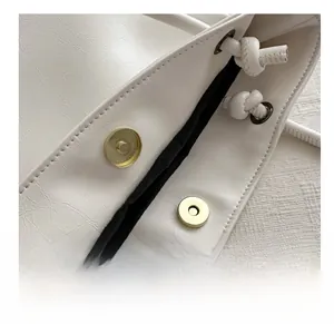 Detail of gold magnetic buckle and soft pleat texture on off-white faux leather tote bag