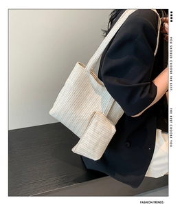 Detail of cream woven straw tote bag and matching zipper pouch worn by a model