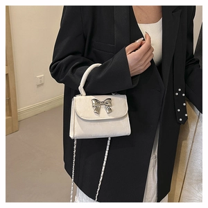 Détail du sac à bandoulière blanc avec nœud argenté et chaîne élégante sur un mannequin