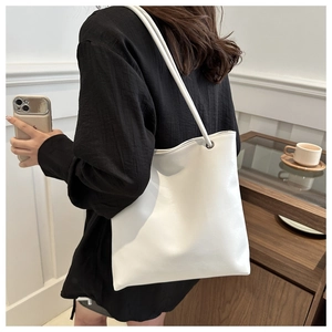 Close-up of white leather tote bag showing smooth texture and slim cylindrical shoulder strap