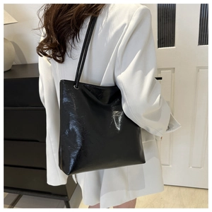 Detail of minimalist black faux leather tote bag with glossy finish on white blazer