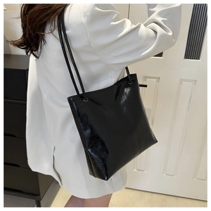 Detail shot of glossy black tote bag texture and slender shoulder straps on model
