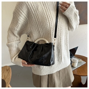 Detail of black pleated cloud bag featuring a pearl handle and crossbody strap design