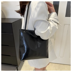 Side view of a large black patent leather tote bag with thin straps on a model