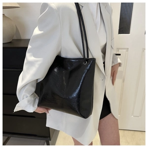 Close-up of a large black glossy tote bag with slim shoulder straps on a fashion model