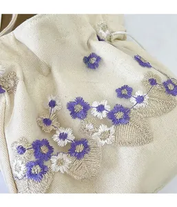 Détail de broderie florale sur sac bandoulière en toile blanc cassé à cordon de serrage