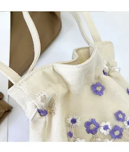 Gros plan de fleurs de marguerite brodées sur un sac en toile crème avec cordon de serrage