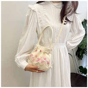 Détail de broderies florales et cordon perlé sur sac seau en toile beige