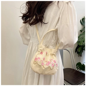 Détail du sac seau en toile beige avec broderies florales et cordon à perles blanches