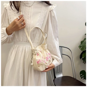 Détail de broderie florale rose sur sac en toile beige avec cordon à perles décoratif