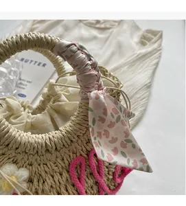 Close-up of straw woven tote bag featuring floral silk scarf handle and pink letter detail