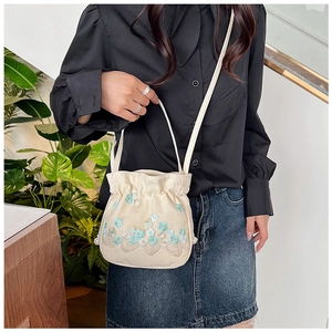 Gros plan sur un sac seau en toile beige avec broderie florale et détails de glands perlés