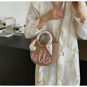 Detail of woven straw bag with pink hello text and floral scarf wrapped handle