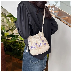 Détail du sac bandoulière en toile blanc cassé avec broderie florale violette et perle