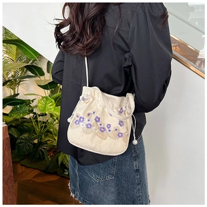 Détails de broderie sur un sac seau en toile crème porté par un mannequin en bandoulière