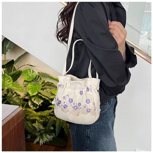Détail du sac seau en toile blanche avec broderies florales violettes et champagne