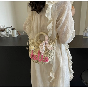 Detail view of woven straw bag with pink hello embroidery and floral handle scarf