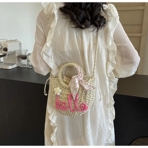 Detail of straw bag featuring pink hello embroidery, white floral accents and floral scarf