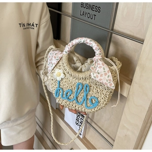 Detail of woven straw beach bag with blue hello embroidery and floral scarf handle