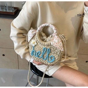 Detail of straw bag featuring blue hello embroidery, floral scarf handle, and inner drawstring