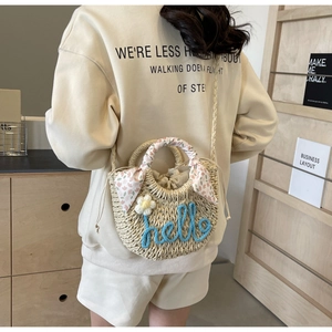 Detail of straw bucket bag with floral embroidery and pink scarf wrapped handle