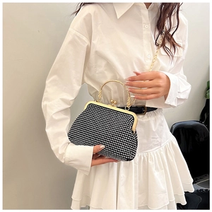 Detail of black rhinestone handbag with gold handle and chain worn with white dress