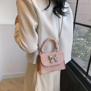 Sac carré en daim rose élégant avec nœud argenté et bandoulière porté par un mannequin