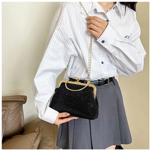 Detail of a black rhinestone shell bag with a gold metal handle and luxury chain strap