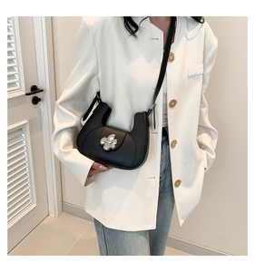 Détail du sac demi-lune noir avec boucle fleur argentée porté sur un blazer blanc cassé