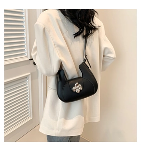 Détail d'un sac hobo demi-lune noir avec fermoir fleur argenté sur un blazer beige