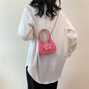 Sac demi-lune rose avec nœud argenté et bandoulière chaîne porté par le modèle