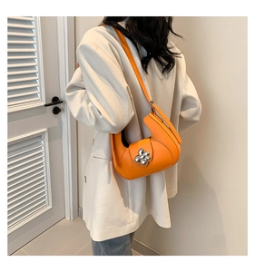 Détail du sac demi-lune orange avec boucle fleurie porté sur une veste beige