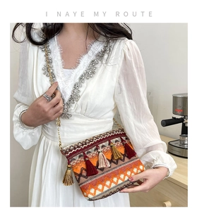 Detail of bohemian woven bag with colorful tassels and gold chain on white dress