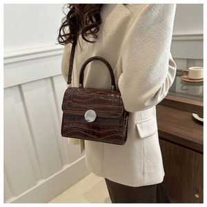 Détail d'un sac bandoulière marron foncé à motif crocodile avec une boucle en métal argenté