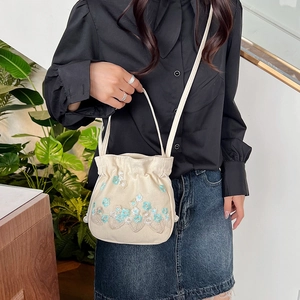 Sac seau beige brodé de fleurs avec cordon porté par un mannequin dans un intérieur