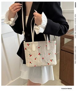 Detail of woven straw tote bag featuring red cherry embroidery and beige leather straps