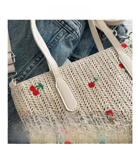 Detail of beige straw tote bag with red cherry embroidery and faux leather handle