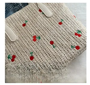 Close-up of woven straw tote bag with red cherry embroidery and leather handle details