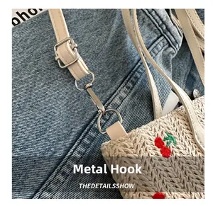 Detail of cherry embroidery on straw bag with silver hardware and adjustable white strap