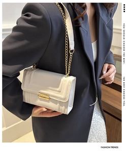 Detail einer cremeweißen Stepptasche mit Kette über einem dunkelblauen Blazer