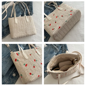Detailed view of straw tote bag featuring red cherry embroidery and leather straps
