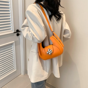 Sac hobo orange avec boucle fleurie argentée porté par un mannequin en veste beige