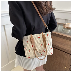 Detail of woven straw tote bag featuring red cherry embroidery and brown leather handles